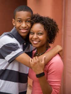 Black teenage boy hugging Black woman, both smiling.