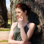 young woman leaning against tree