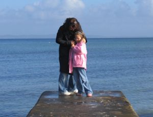 mother and daughter hug on shoreline