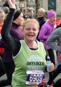woman running half marathon for amaze raises hand in air