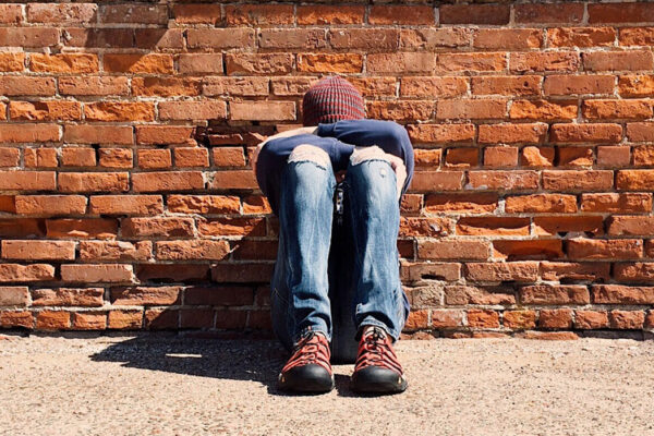 young man sits against wall with head on knees