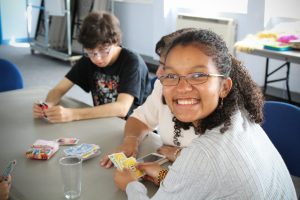 Young woman grins while playing card game with other young people