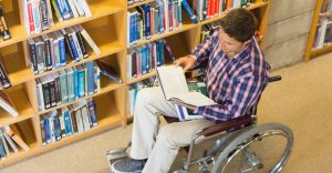 young male wheelchair user looks at book in university library