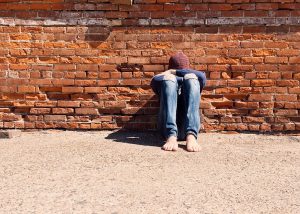 young person sitting against a wall