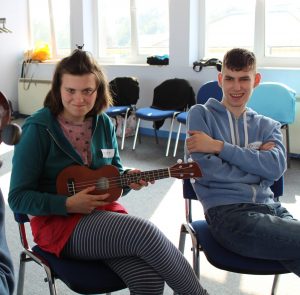 young woman playing small guitar, sat next to a young man