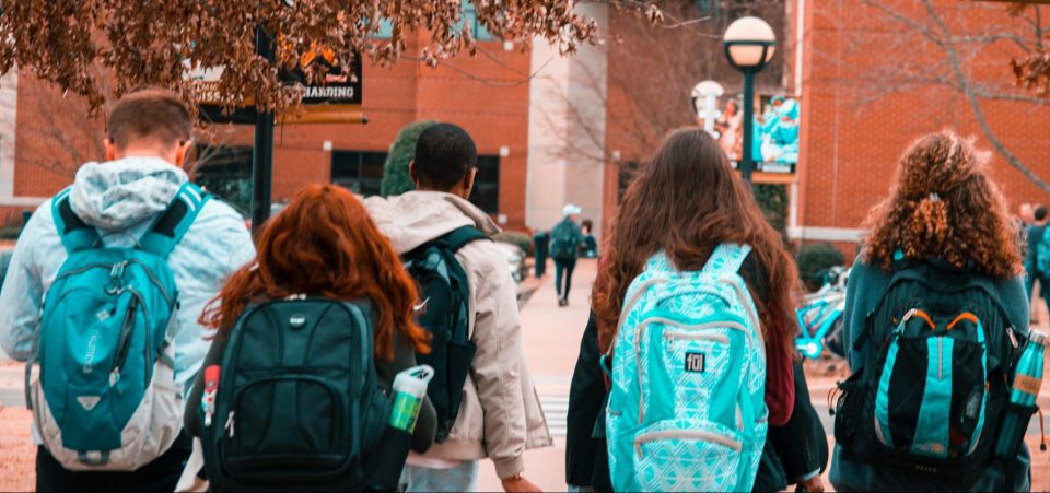 young people wearing backpacks facing away from the camera and heading toward a large brick building