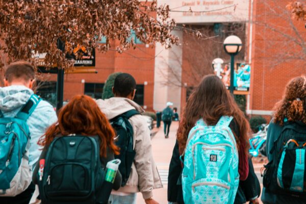 young people wearing backpacks facing away from the camera and heading toward a large brick building
