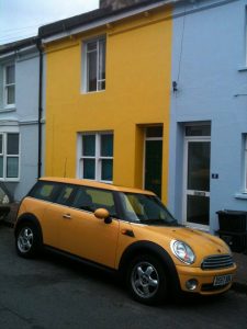 yellow Ford Mini car in front of a yellow house