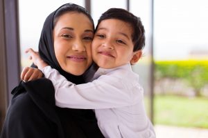 smiling woman in a hijab being hugged by her young son