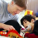 boy with prosthesis on jaw playing with dinosaur toys with middle-aged man