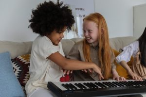 two girls playing a keyboard together, one smiling broadly