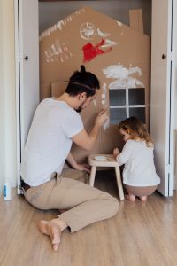 man painting cardboard house with child