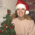 CEO Rachel Travers, a middle-aged woman with long light brown hair smiling widely and wearing a santa hat, next to a small christmas tree