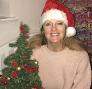 CEO Rachel Travers, a middle-aged woman with long light brown hair smiling widely and wearing a santa hat, next to a small christmas tree