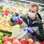 Man in supermarket wearing a mask and putting an apple in a bag