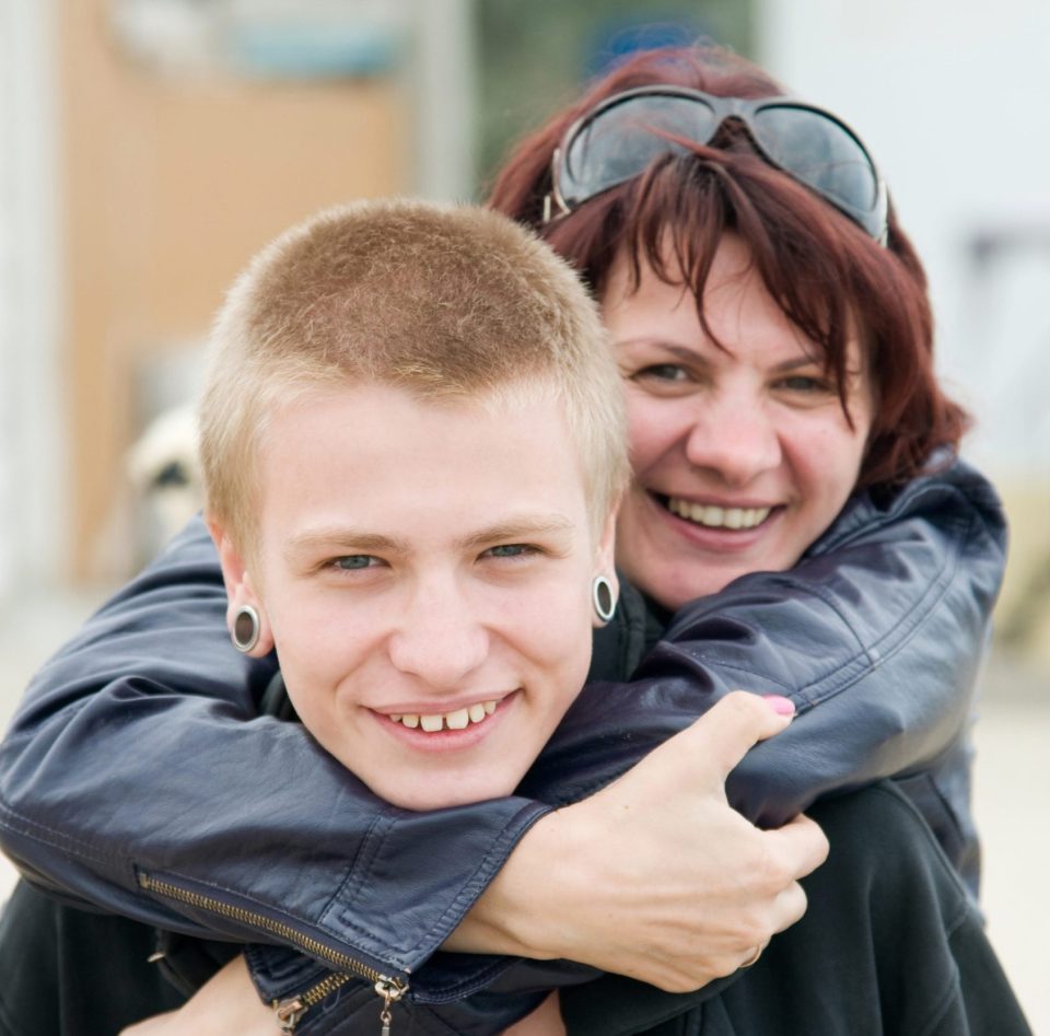 middle aged woman smiling with her arms round a teenage boy