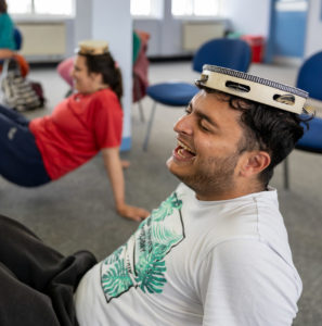 young people playing a game on the floor with tambourines on their heads, laughing