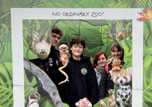 Young people from Amazing Futures pose in a big cut out frame like a polaroid photo in a rainforest with lots of animals, that says "Me and my wild friends" along the bottom