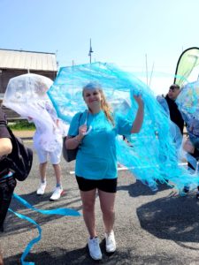 Smiling young woman in a blue Amazing Futures t-shirt, holding her jellyfish umbrella with tendrils, which is the same colour