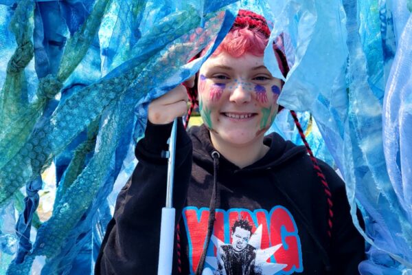 Smiling young person with short dyed hair holding an umbrella decorated like a jellyfish with long translucent blue tendrils