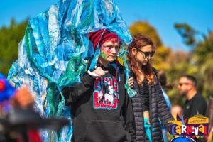 Young person with dyed hair and alternative clothing holding their jellyfish umbrella over one shoulder. It looks sunny.