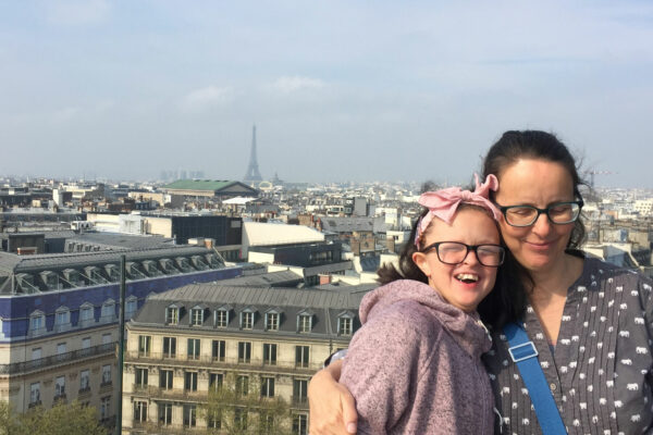 Mum and her older daughter, both wearing glasses, standing on a roof terrace in Paris, with Eiffel tower in background.