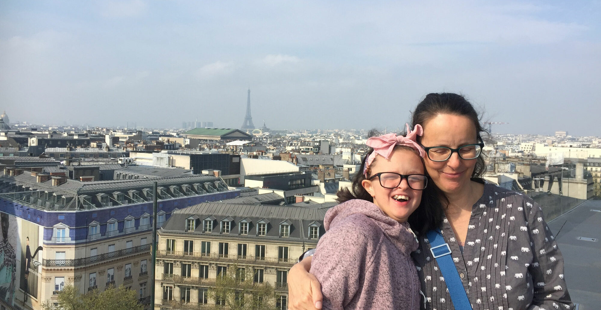 Mum and her older daughter, both wearing glasses, standing on a roof terrace in Paris, with Eiffel tower in background.