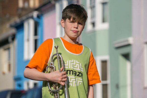 12 year old boy in Amaze vest holds trumpet outside Hanover houses.
