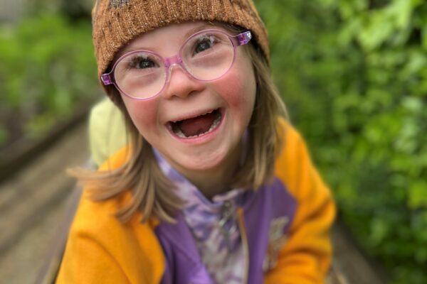 Young girl with down syndrome seated outdoors, smiling broadly