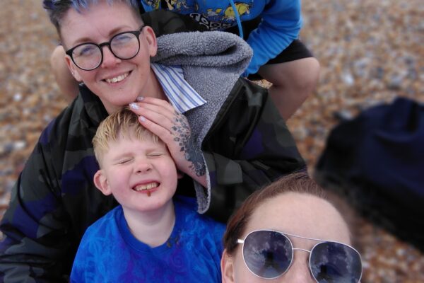 Two mums and their two sons taking a happy family selfie on a cloudy Sussex beach.