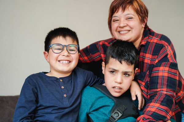 Mother and her two sons hugging on sofa and smiling. Middle child has a disability.