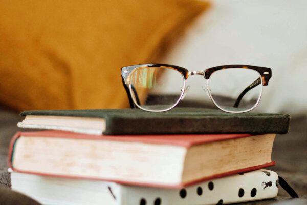 A pair of spectacles balance upon 3 books.