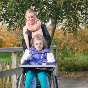 Young woman carer pushes disabled girl in a wheelchair outdoors