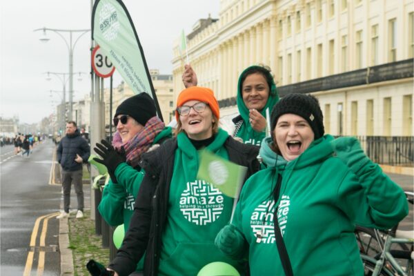 Four staff in Amaze hoodies cheer Brighton runners on seafront road