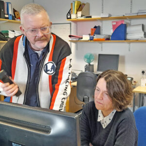 Two advice workers discuss a call in front of a computer.