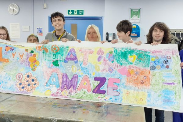 young people hold up a colourful banner that says "From all of us at Amaze"