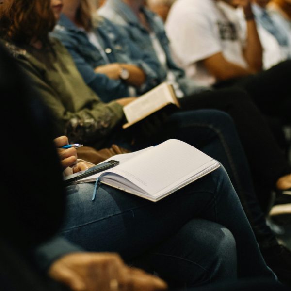 Group of people seated in a training session. Their notebooks are open on their laps.