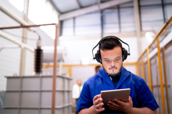 young man with down syndrome wearing headphones looks at a table while working in a warehouse.