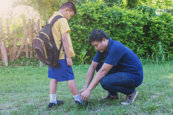 father bends down to tie son's shoelaces outdoors